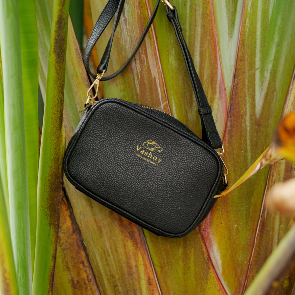 Black Vashoy vegan crossbody bag hanging against a colorful tropical plant