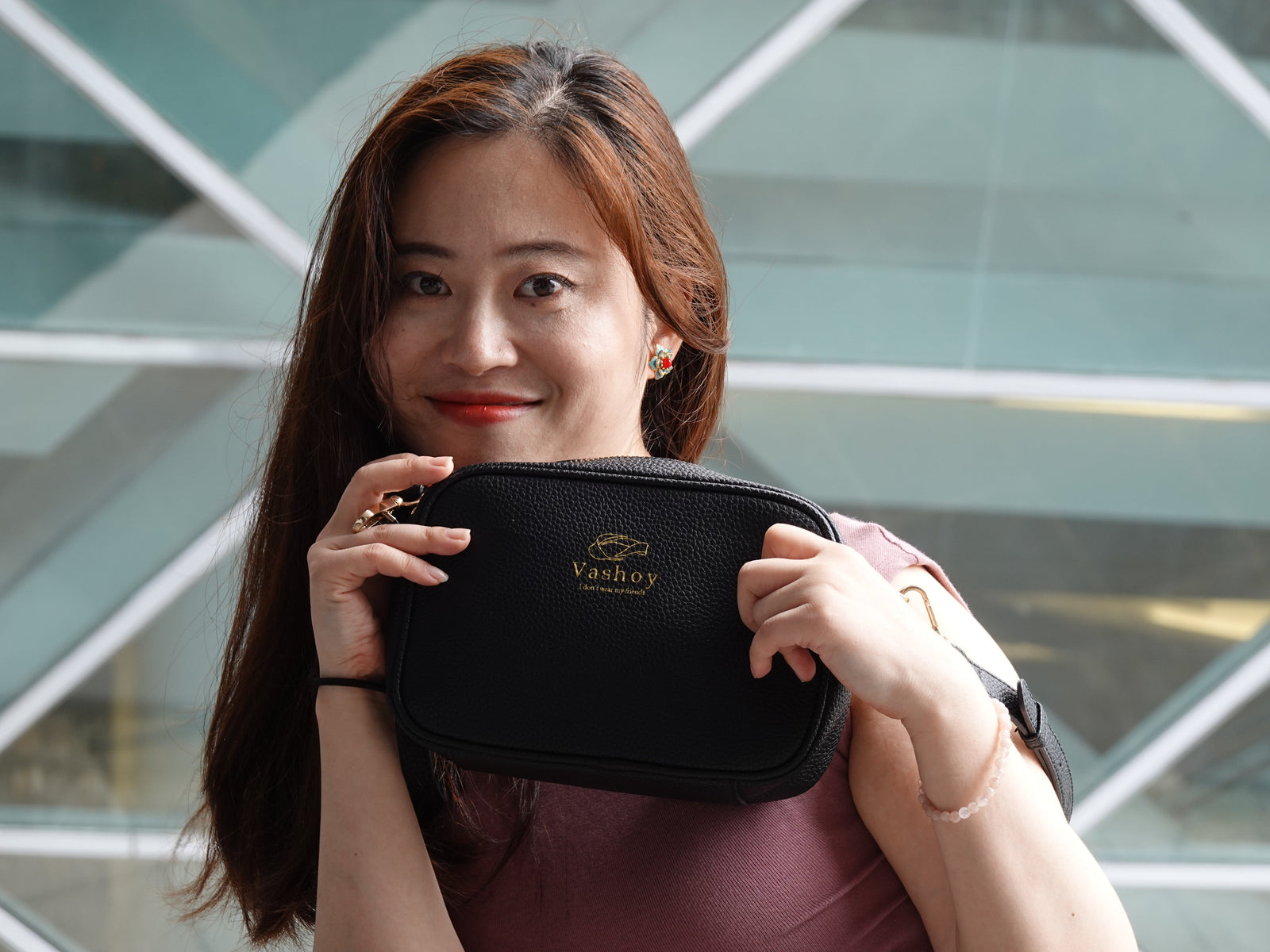 Woman holding a black Vashoy vegan crossbody bag made with pineapple leaf fiber, showing its textured surface and gold logo.